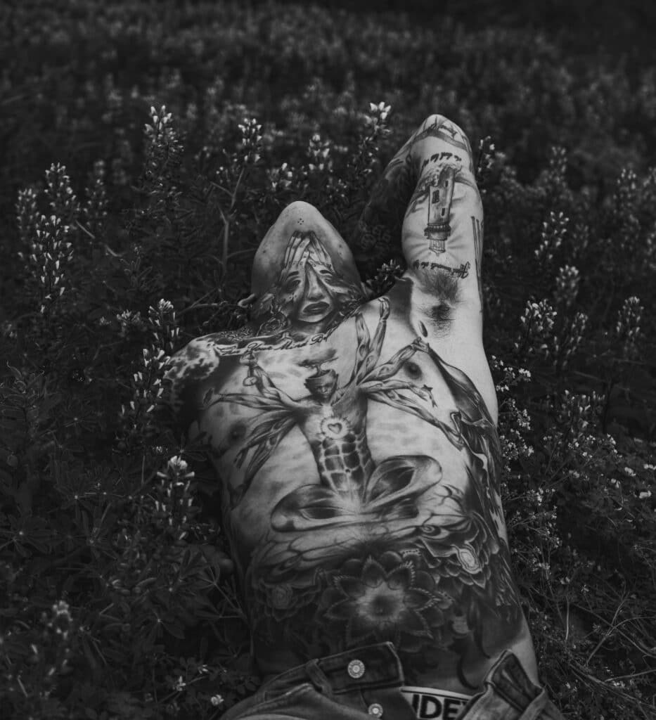 full chest and neck tattoos on man laying in field