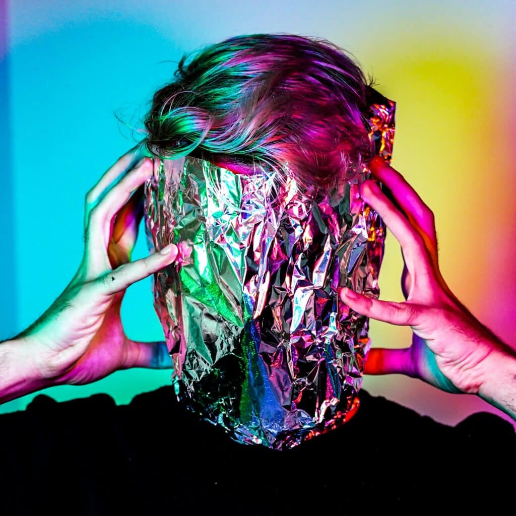 portrait of a person with aluminum foil over their face their hands and and hair colored by neon lights