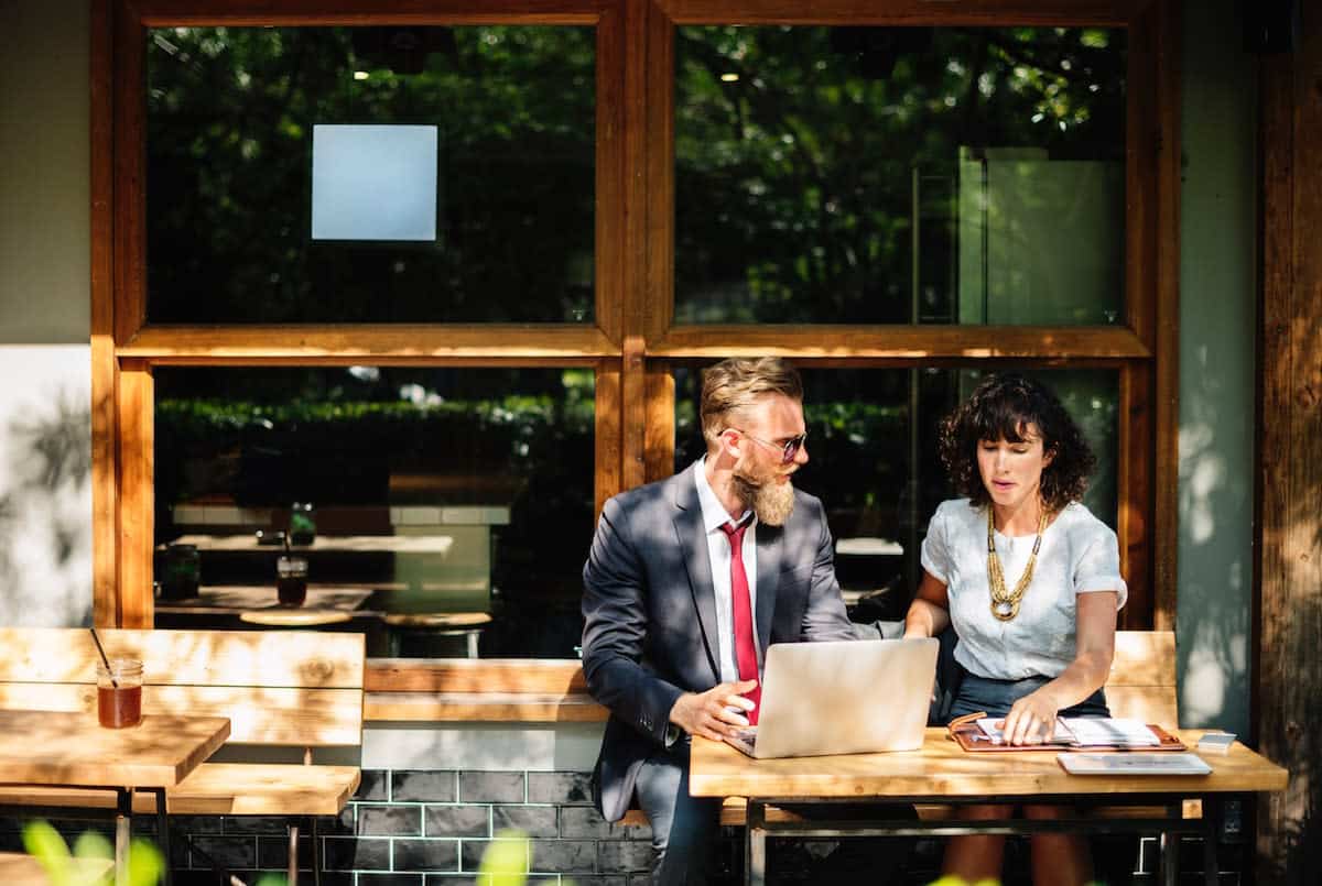 man and woman sitting at an outdoor table together talking and looking at laptop