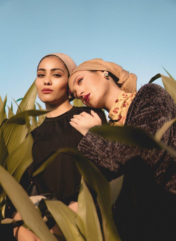 two women posing black dresses surrounded by tall green plants