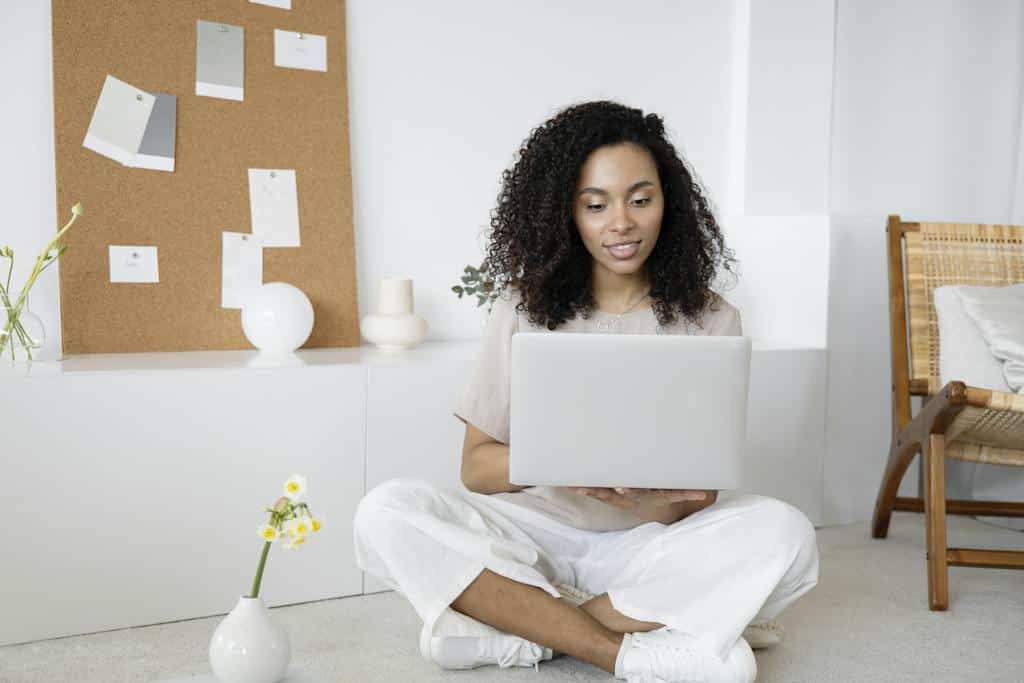 woman in white dress shirt and white pants sitting on floor using macbook